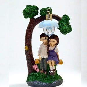 Cute figurine of a boy and girl sitting under a flower-shaped lamp on a bench beside a tree