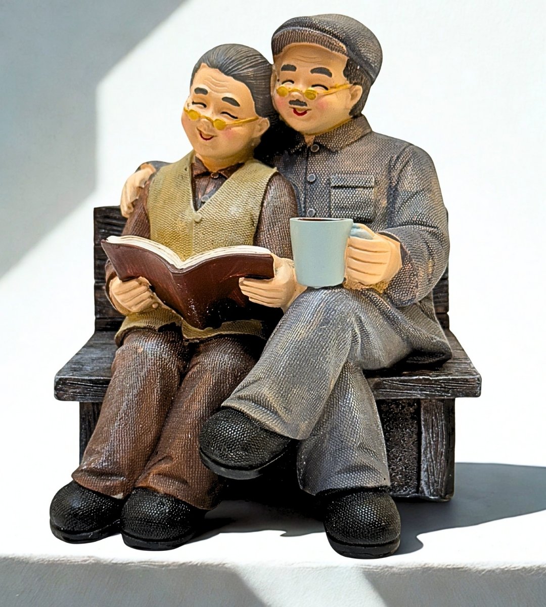 Elderly couple figurine sitting on a bench, reading together and enjoying a peaceful moment of love